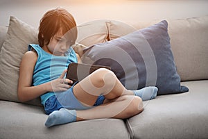 Little Arabian boy sitting on sofa and playing game on digital tablet