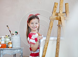 Little artist girl holding a paintbrush and looking over a canvas