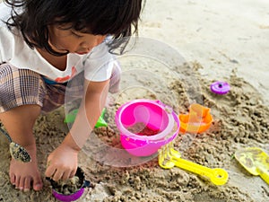 Little Asia girl sitting in the sandbox and playing whit toy shovel bucket