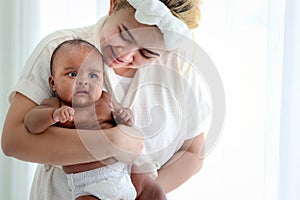 Little Asian African newborn baby girl in the embrace of her mom, portrait of sweet adorable infant in arms of mother, parent