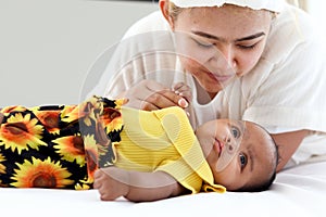 A little Asian African newborn baby girl lying on white bed with mother holding her hand, mother showing love and care to new