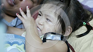 Little Asian baby girl, 2 years old, keeping her thumb in mouth, while the mother reading a bedtime story for her