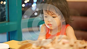 Little Asian baby girl, 2 years old, paying no attention to the meal, losing appetite, as she was addicted to a smartphone