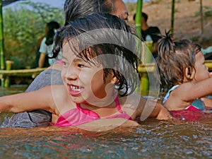 Little Asian baby girl, 3 years old, enjoys playing water in a river with her auntie and little sister