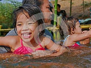 Little Asian baby girl, 3 years old, enjoys playing water in a river with her auntie and little sister - playing outdoor and