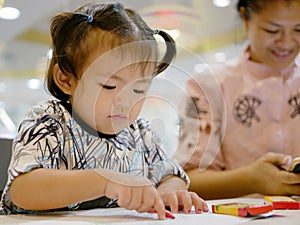 Little Asian baby girl being left alone with crayons, while her mother ignoring her and solely focusing on the smartphone