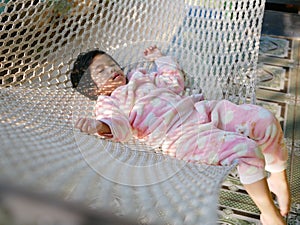 Little Asian baby girl comfortably lying down on a hammock with the morning sunlight