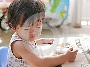 Little Asian baby girl enjoys eating food by herself