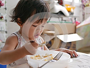 Little Asian baby girl enjoys eating food by herself