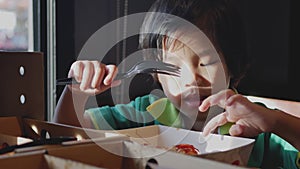 Little Asian baby girl enjoys eating tomato sauce on a piece of pizza by hand and fork by herself at a restaurant