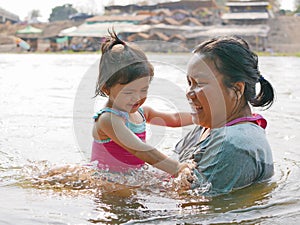 Little Asian baby girl enjoys playing water in a river with her auntie