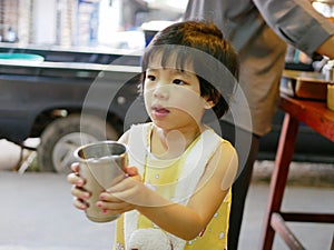 Little Asian baby girl helping her auntie carrying cups of water to serve other family members