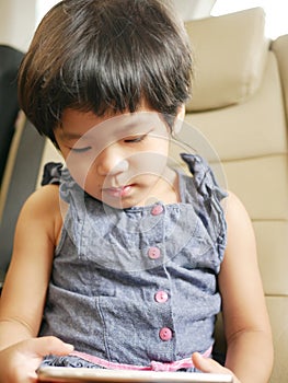 Little Asian baby girl holding and using a mobile phone, while sitting in a driving car