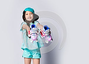 Little asian baby girl kid sitting with roller skates in light blue t-shirt and hat cap happy smiling on white
