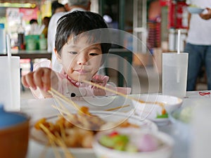 Little Asian baby girl learning to eat pork satay by herself