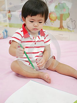 Little Asian baby girl learning to hold a pencil and drawing on a book