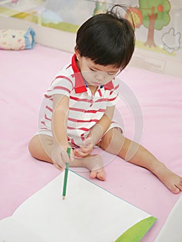 Little Asian baby girl learning to hold a pencil and drawing on a book