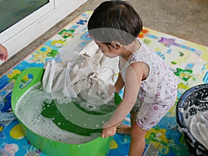 Little Asian baby girl learning to wash clothes at home