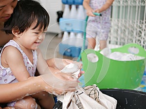 Little Asian baby girl learning to wash clothes at home