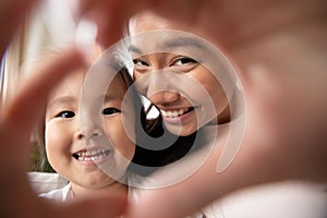 Little asian baby girl making heart gesture with smiling mom.