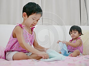 Little Asian baby girl, 18 months old, her older sister folding clothes and try to do the same thing