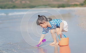 Little asian baby girl playing sand on the beach. Kid three years old play with sand toys