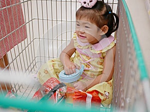 Little Asian baby girl sits in a shopping cart, enjoys doing shopping with her mother