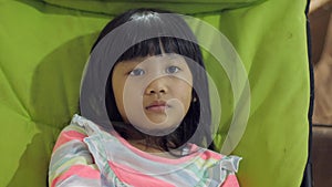 Little Asian baby girl sitting on green chair while watching tv television