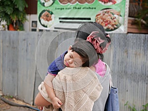 Little Asian baby girl sleeping on a shoulder of her auntie walking in a small alley