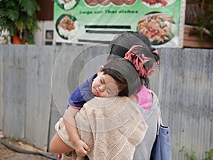 Little Asian baby girl sleeping on a shoulder of her auntie walking in a small alley photo