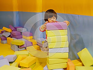 Little Asian baby girl stacking up foam building bricks / blocks at an indoor playground