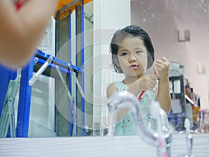 Little Asian baby girl tring to open a toothpaste cap in front of a mirror by herself