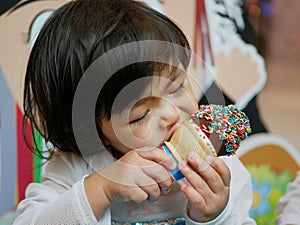 Little Asian baby girl, 2 years old, feeling blissful eating / biting ice cream cone photo