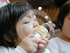 Little Asian baby girl, 2 years old, feeling blissful eating / biting ice cream cone - facial expression of joyfulness photo
