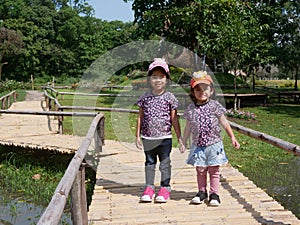 Little Asian baby girls, sisters, 3 and 2 years old, smiling and making cute pose together for outdoor photo shoot
