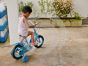 Little Asian baby learning to ride a bicycle with training wheels at home