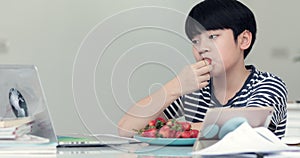 Little asian boy eats strawberries and Using Notebook at Home.