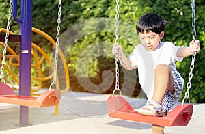 Little Asian boy having fun on a swing on the playground in public park on autumn day