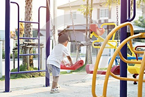 Little Asian boy having fun on a swing on the playground in public park on autumn day