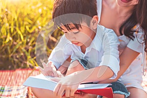 Little Asian boy and his mother reading tale story books at meadow field. Mother and son learning together. Celebrating in Mother