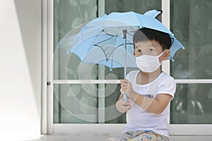 Little Asian boy holding an umbrella and wearing face mask protection from coronavirus illnesses