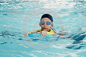 Little asian boy learn swimming in pool and swim using foampad