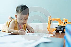 Little Asian boy lying on the floor drawing with pencil