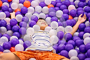 Little asian boy playing in ball pit playground with purple and white ball