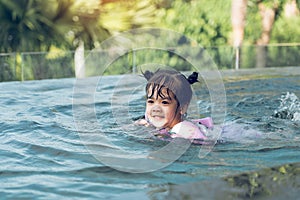 Little asian boy plays in the water while swimming in the pool wearing armbands