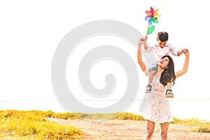 Little Asian boy riding back on his super power mom in meadow near lake. Mother and son playing together. Celebrating in Mother