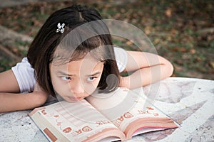 Little Asian child boring lessons reading a book