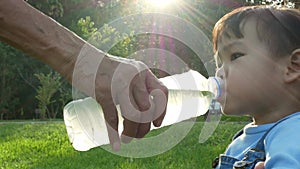 Little Asian child girl drinking some water from bottle in the garden