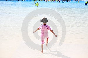 Little Asian child girl enjoys and running into big Swimming pool outdoor on holidays. Rear view children having fun