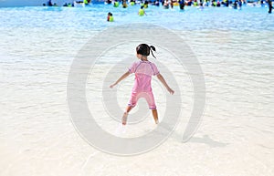 Little Asian child girl enjoys and running into big Swimming pool outdoor on holidays. Rear view children having fun